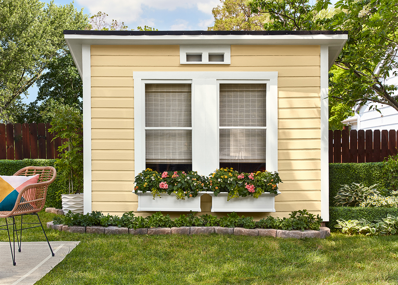 Backyard shed with white-trimmed windows and planters. Its horizontal siding is painted in Soft Candlelight.